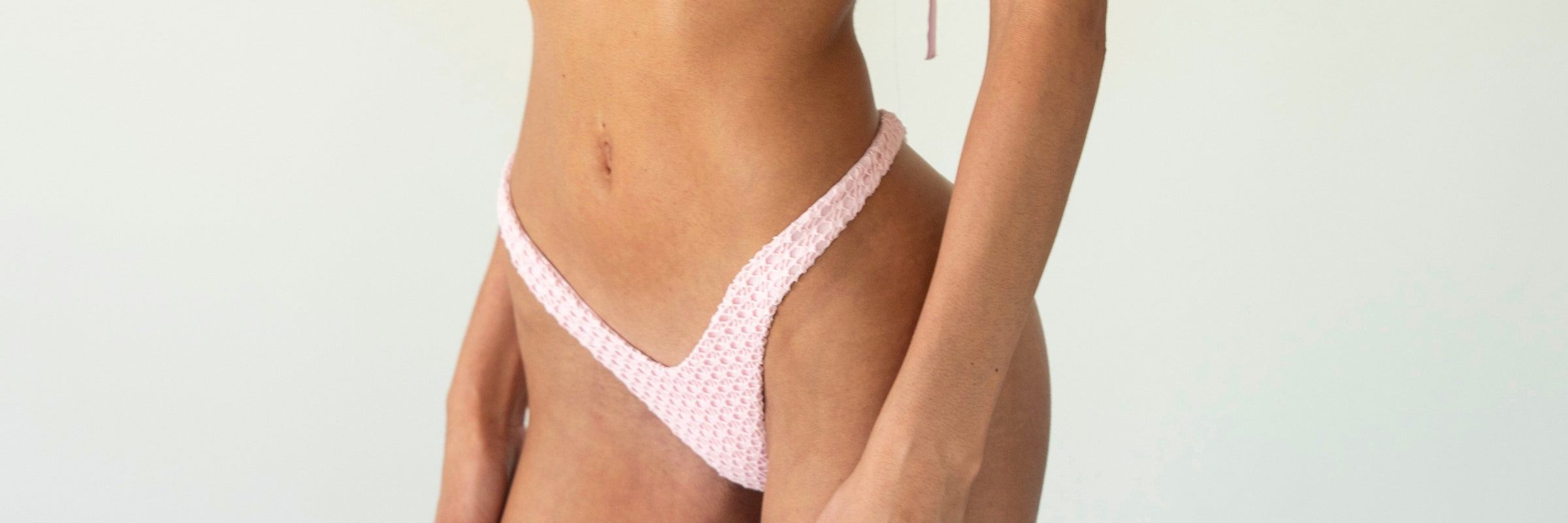 A close-up of a model wearing a light pink and white patterned thong-style underwear bottom against a plain light background.